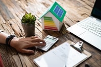 main-maison-miniature-dpe-panneaux-solaires-bureau-calculette-plante-ordinateur-portable